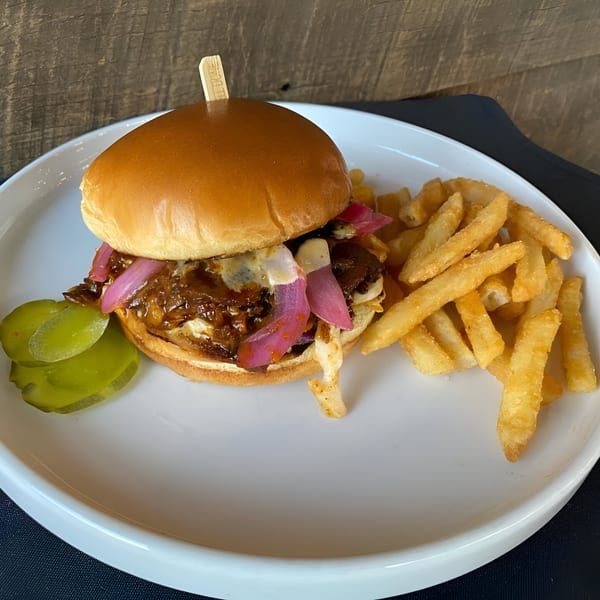A BBQ pulled pork sandwich with pickled onions, melted cheese, and a side of fries and pickles.