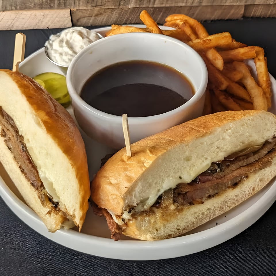 French dip sandwich with fries, au jus, and a side of horseradish sauce and pickles.