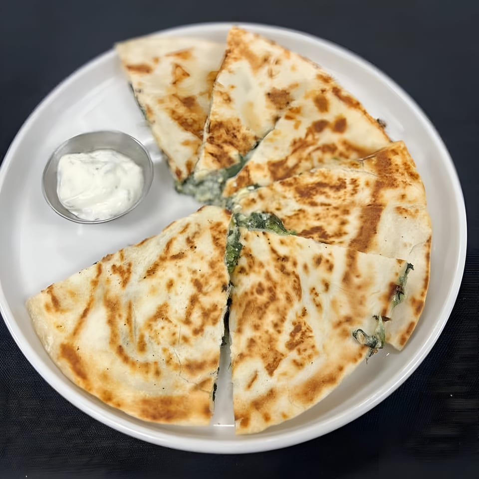 Spinach and cheese quesadilla wedges with a side of sour cream on a white plate.