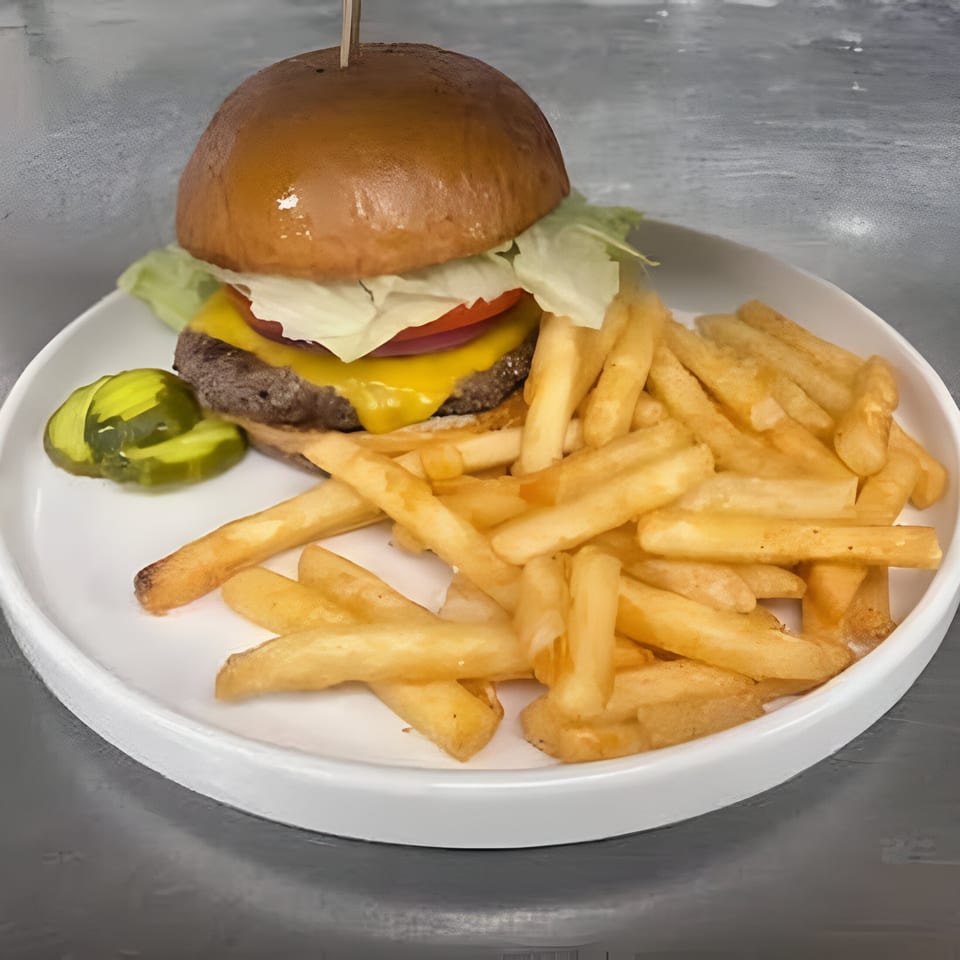 A cheeseburger with lettuce, tomato, and pickles, served with a side of golden fries.