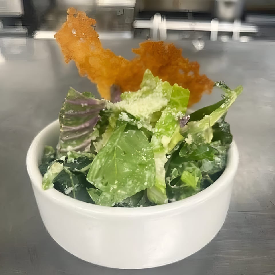 A Caesar salad with green lettuce, dressing, grated cheese, and a large cheese crisp in a white bowl.