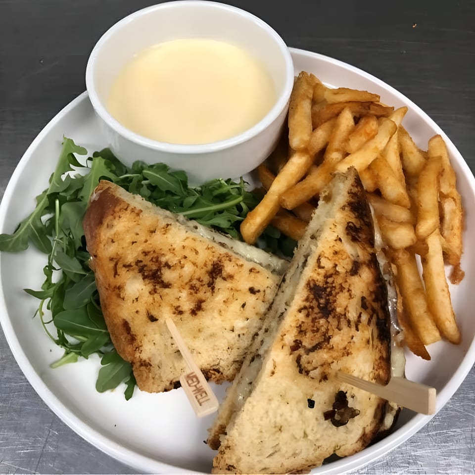 Grilled cheese sandwich with fries, a side of cheese sauce, and arugula on a white plate.