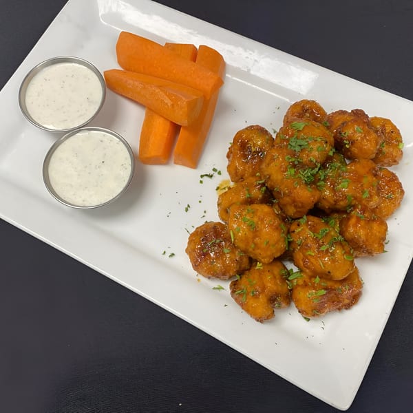 A plate of golden-brown boneless wings with parsley, two ranch cups, and carrot sticks.